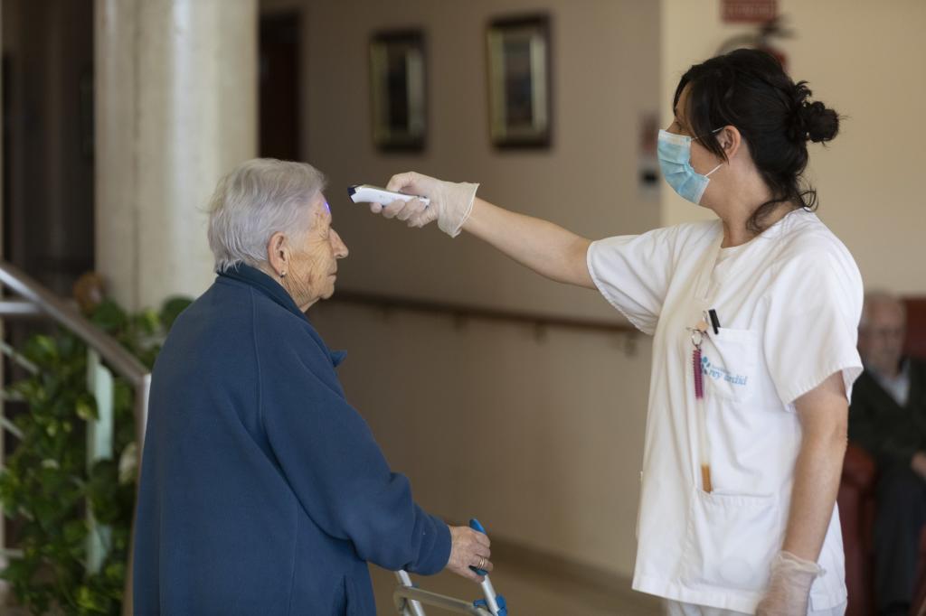 Una enfermera le toma la temperatura a una anciana en una residencia.
